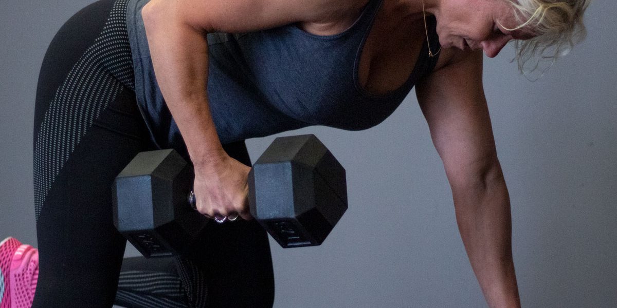 personal trainer doet dumbbell row op een bankje